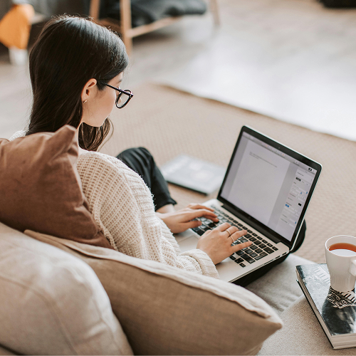 Frau sitzt auf der Couch und arbeitet mit ihrem Laptop
