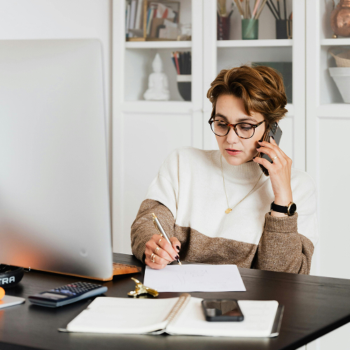 Frau sitzt im Büro am Arbeitstisch und telefoniert mit dem Handy